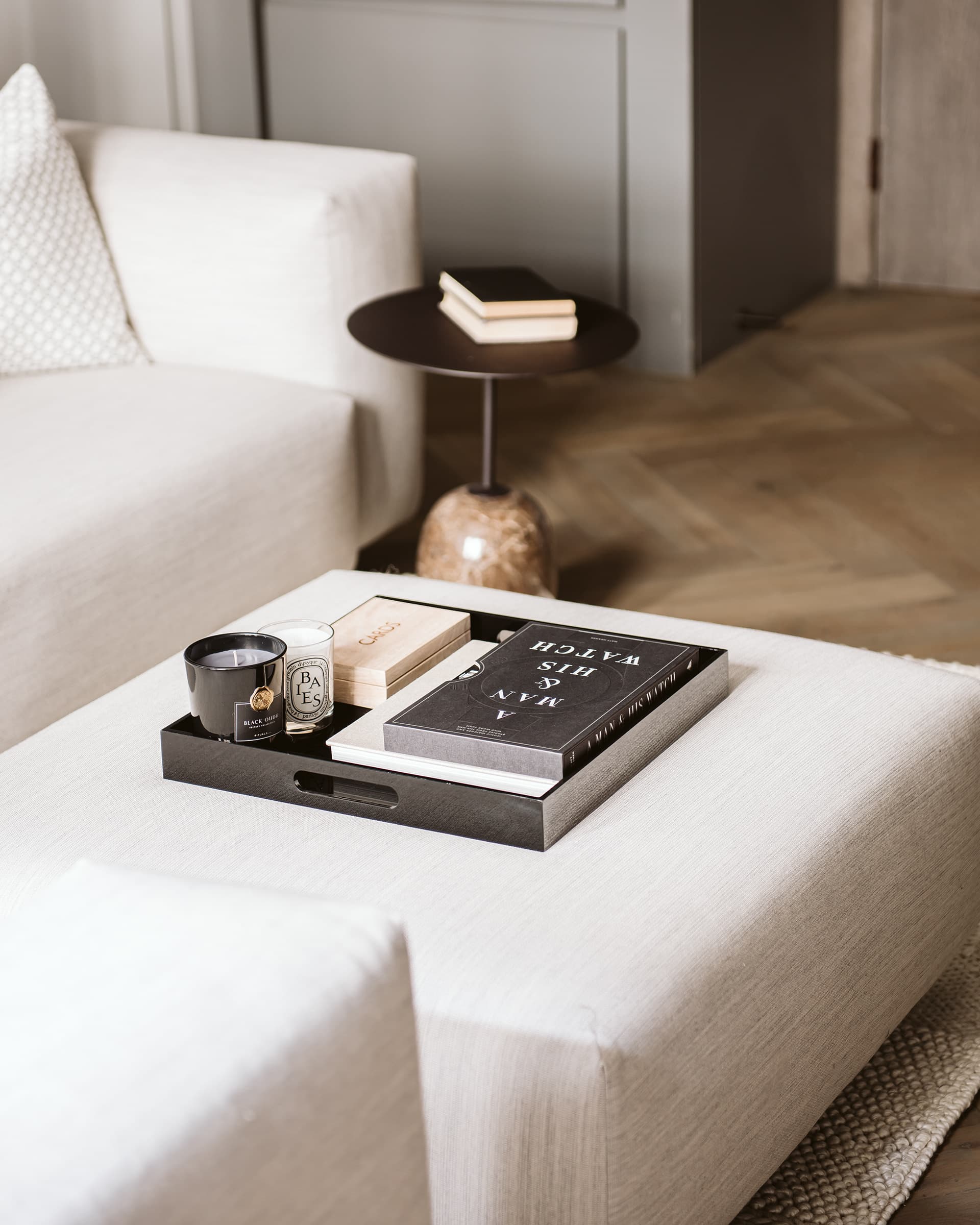 Styled ottoman tray with Diptyque candle, design books and marble side table