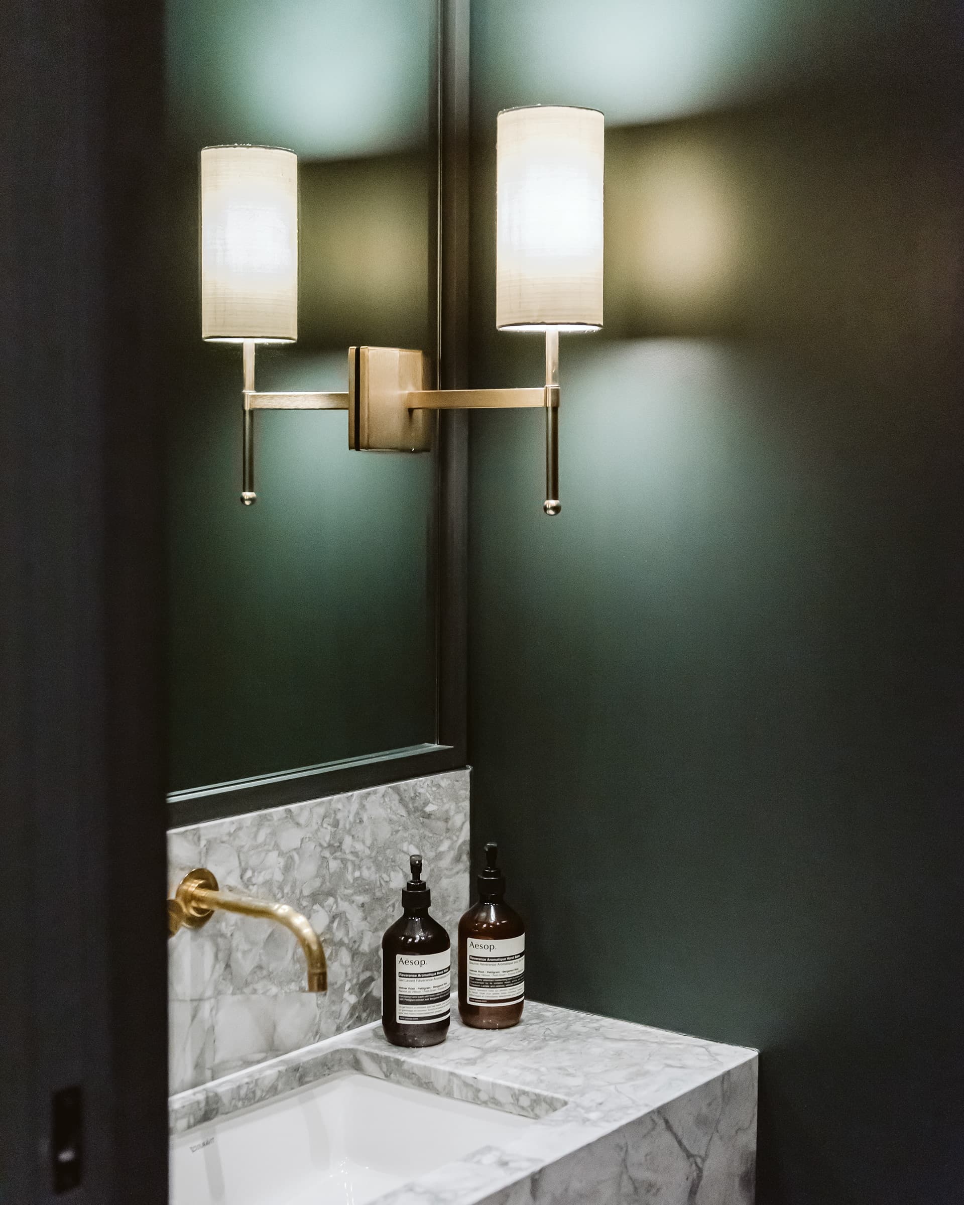 Deep green bathroom with brass twin wall lights and marble basin