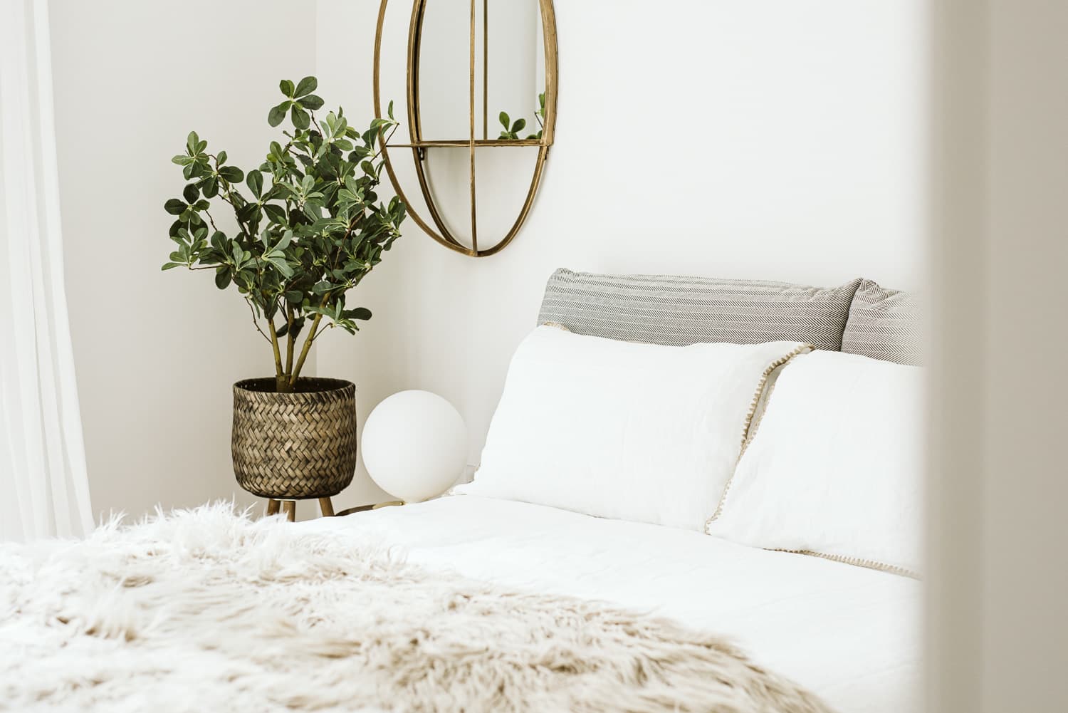 Styled bedroom with plant in basket pot, brass mirror and white linen