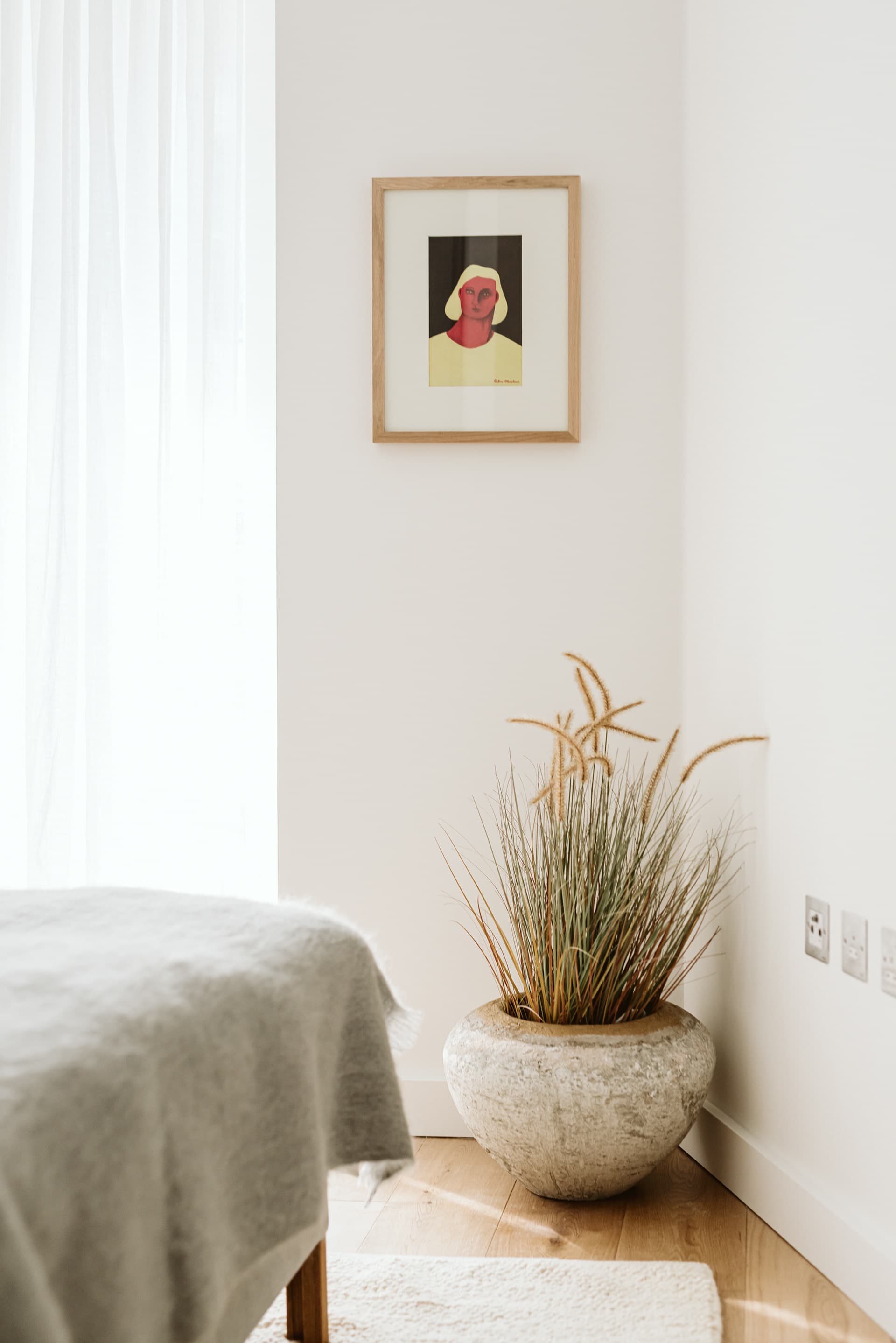 Bedroom corner with stone planter, framed portrait art and natural linen