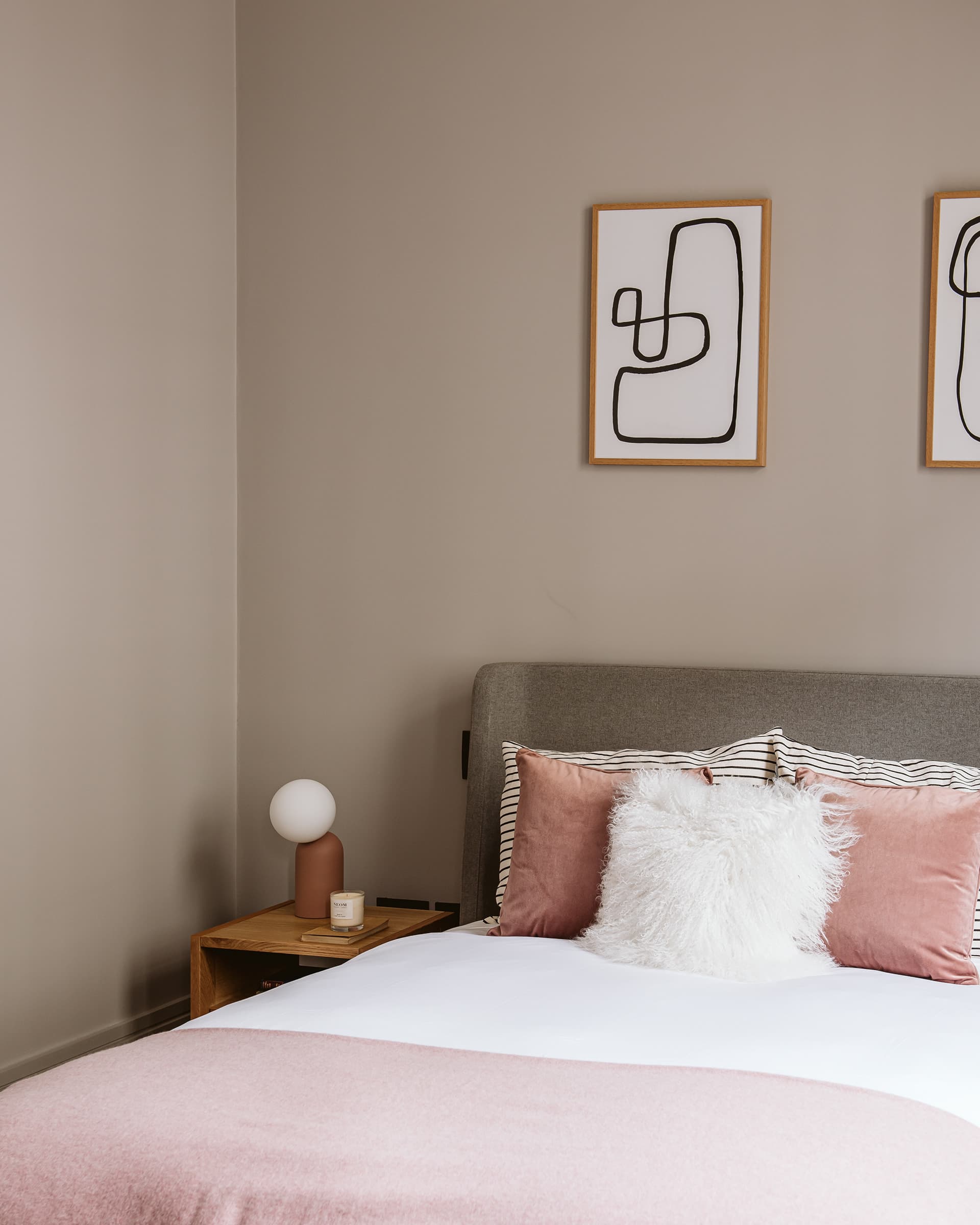 Blush-toned bedroom with abstract framed prints and velvet cushions