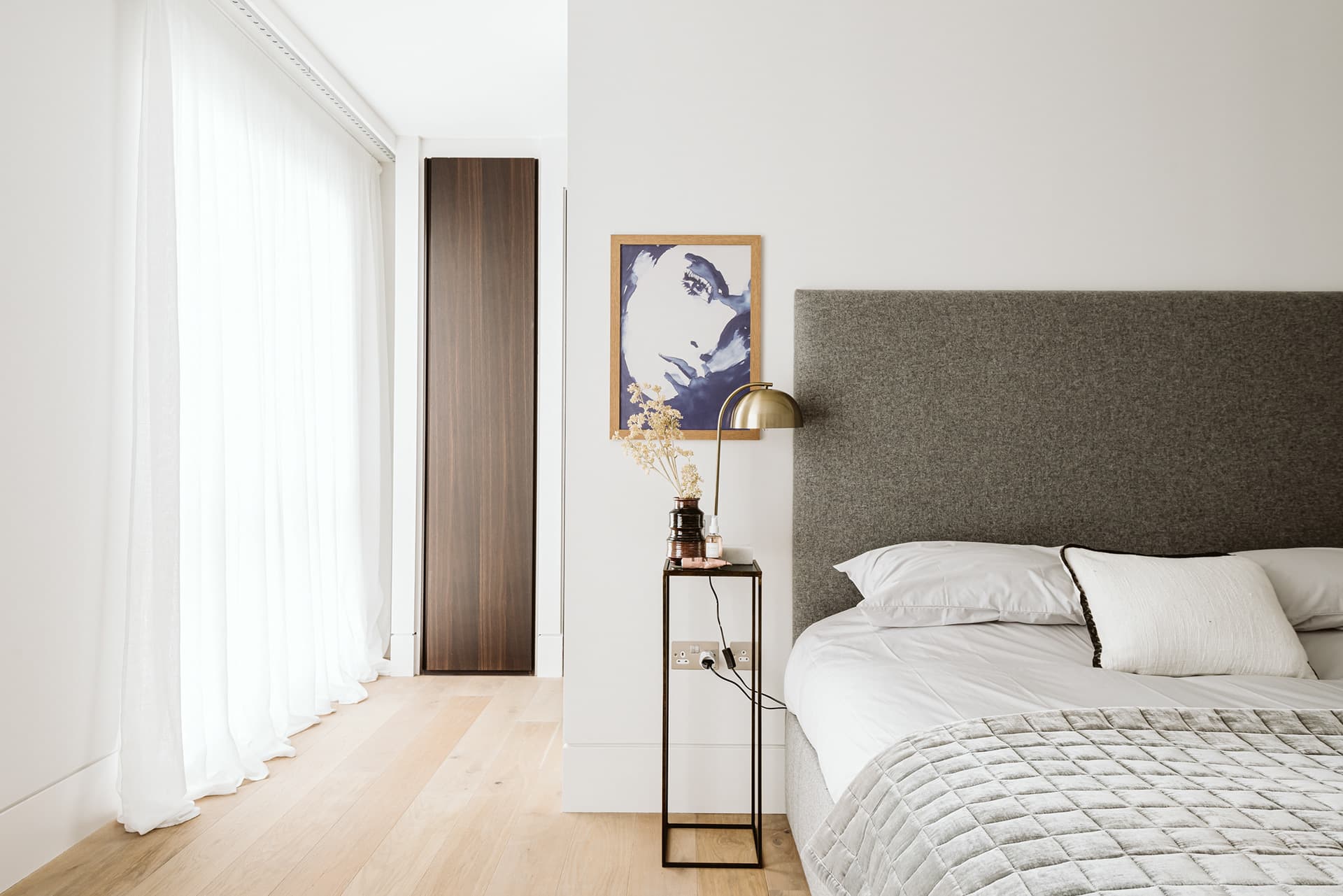 London bedroom styled with upholstered grey headboard and brass lamp